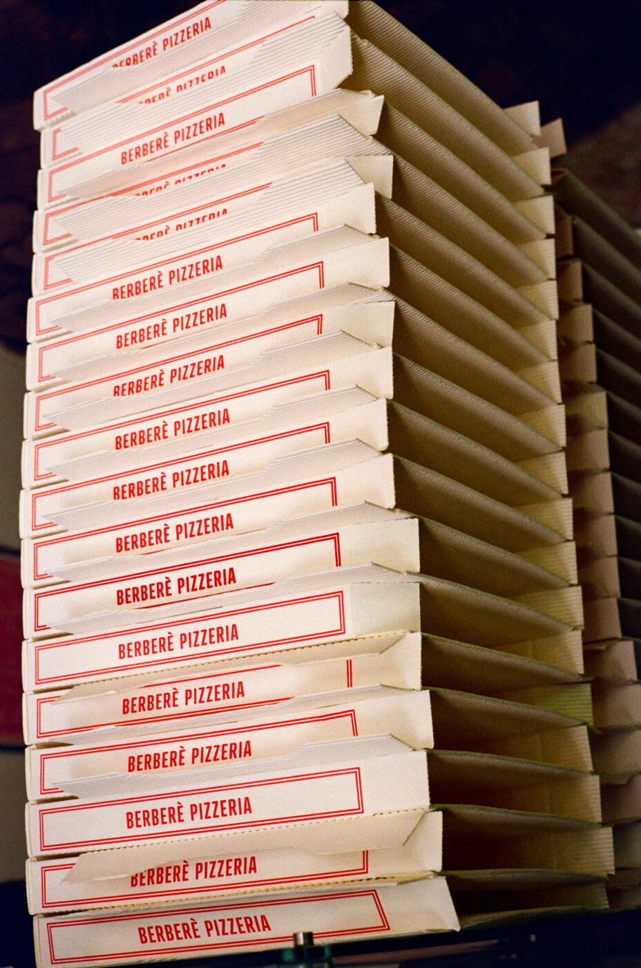A stack of white pizza boxes with red BERBERE PIZZERIA logos, neatly arranged and ready for use.