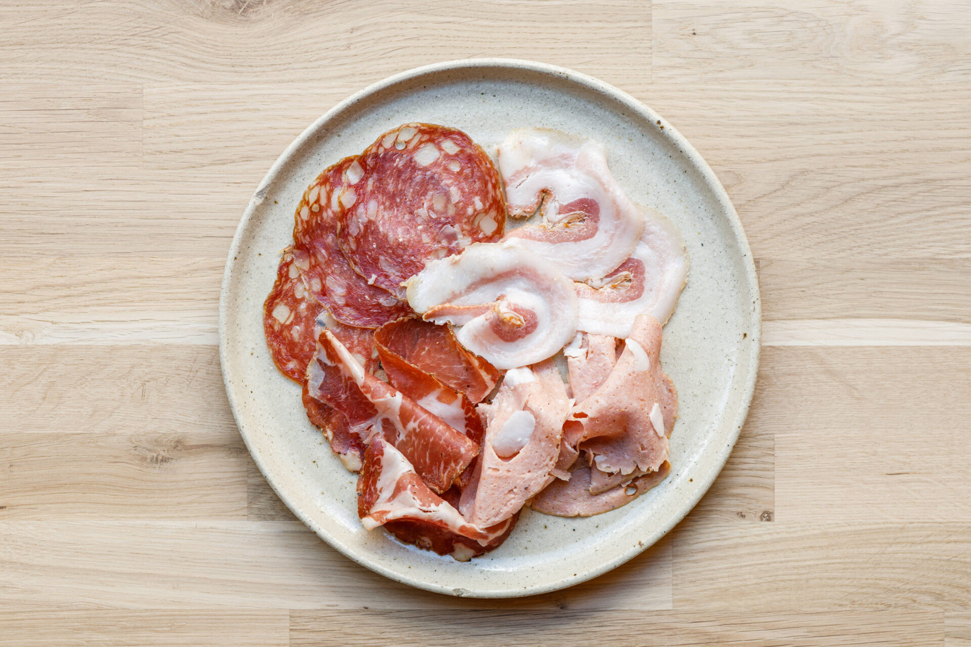 A plate with assorted sliced cured meats like salami and prosciutto, arranged in a small pile on a wooden surface.