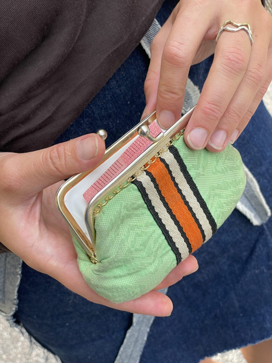 A person with a wavy silver ring opens a green coin purse with black, white, and orange stripes, showing cards inside.