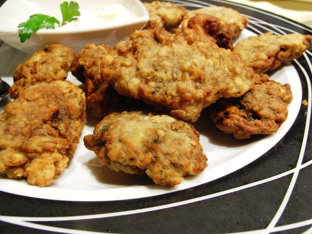 A plate of crisp golden-brown fried mushrooms with creamy dip and parsley garnish.