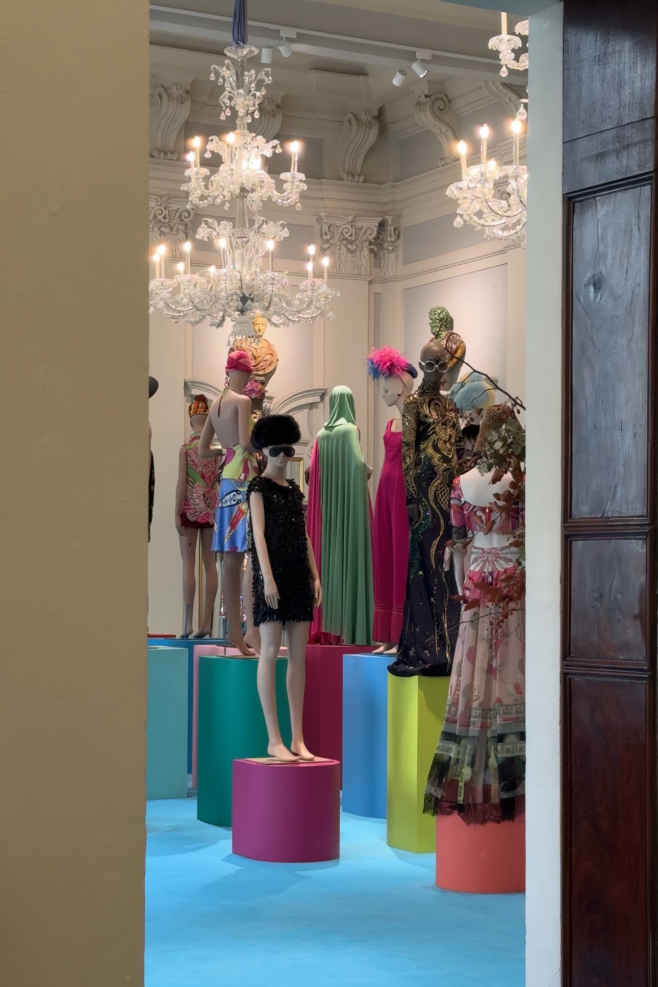 A mannequin stands in a room beneath a sparkling chandelier.