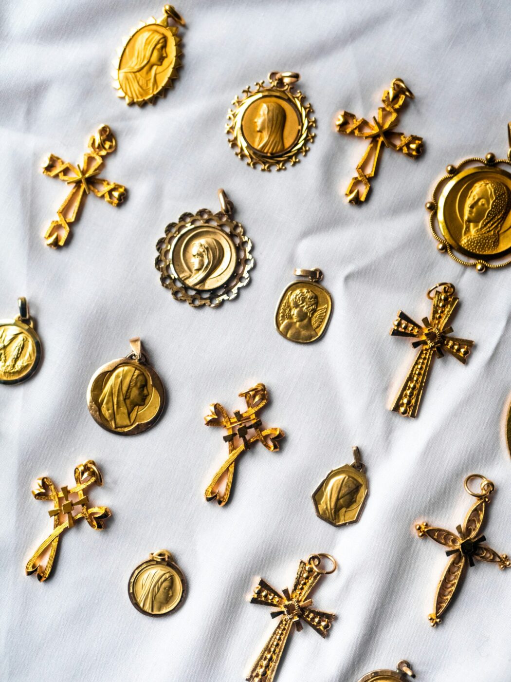 A collection of gold religious pendants—crosses and saint medallions—arranged on white fabric.