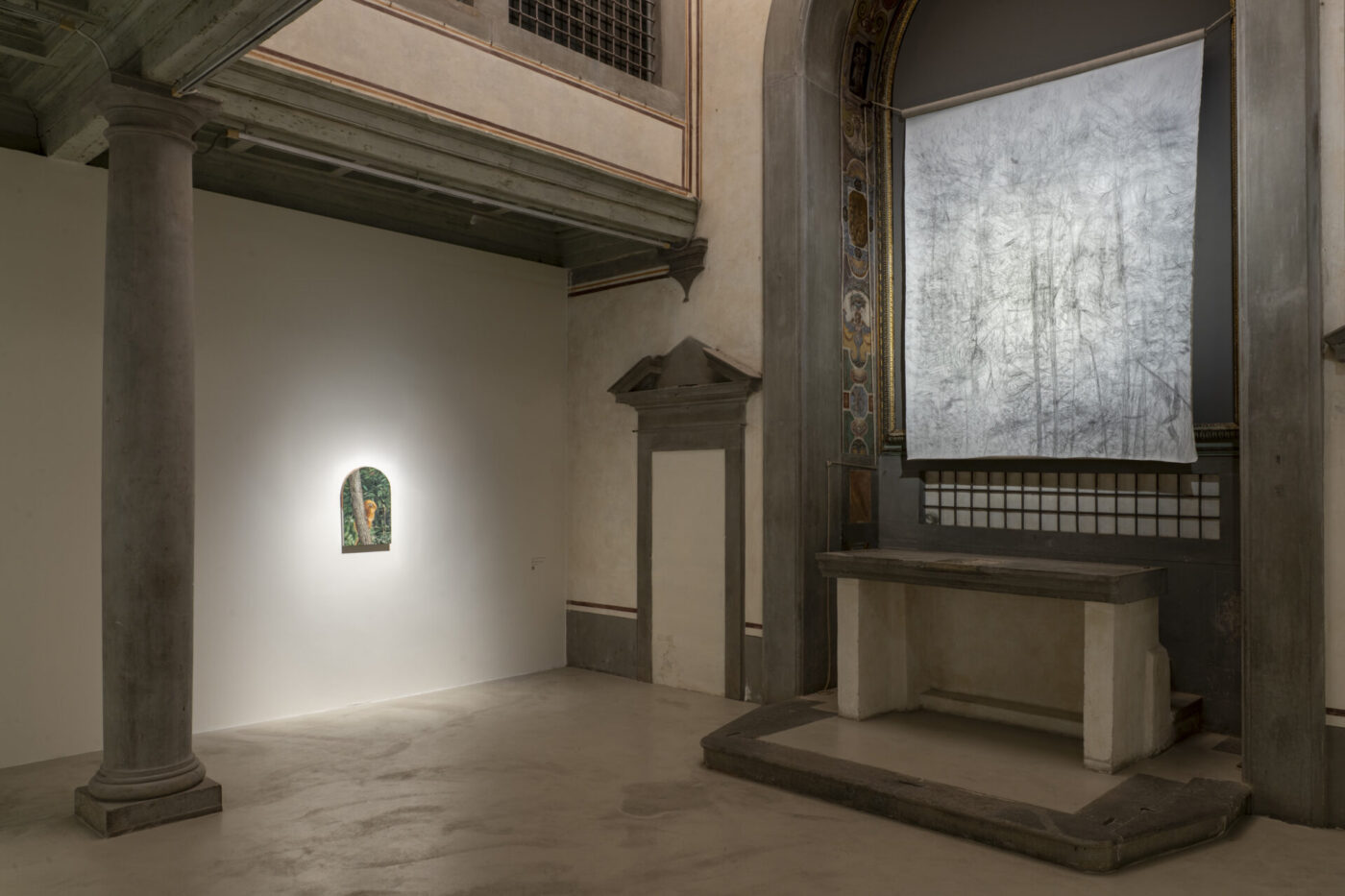 A gallery with classical columns, a small painting on a white wall, and textured silver art above an ornate altar. Soft lighting throughout.
