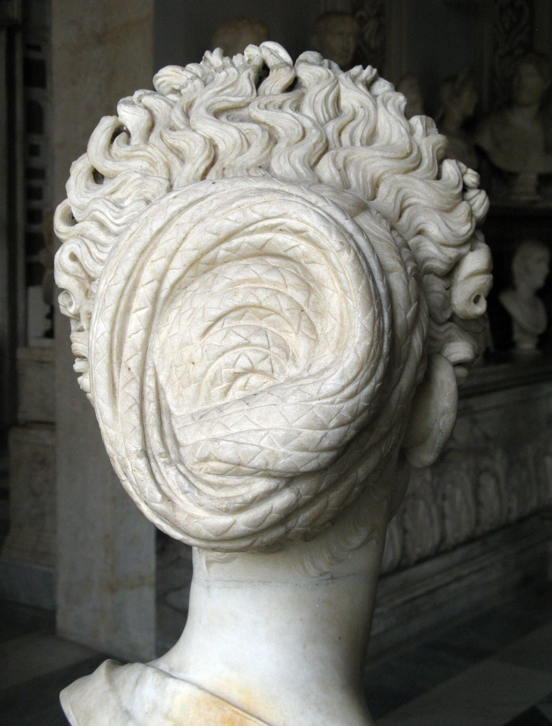 A marble statue of a woman from behind, with intricately braided hair in a bun, showcasing fine texture and expert craftsmanship.