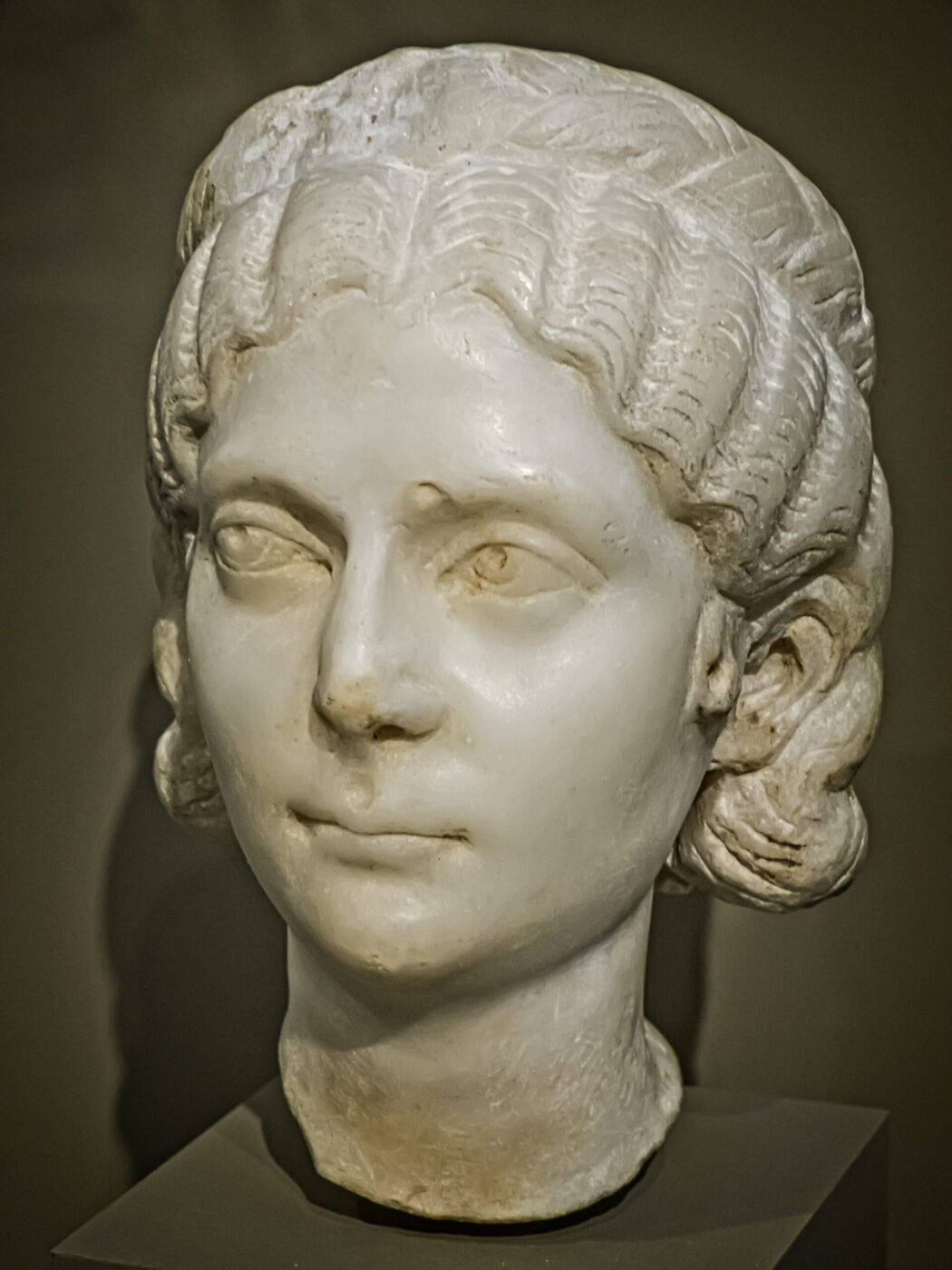 Marble bust of a woman with center-parted wavy hair in soft curls, calm expression, and detailed features against a neutral background.