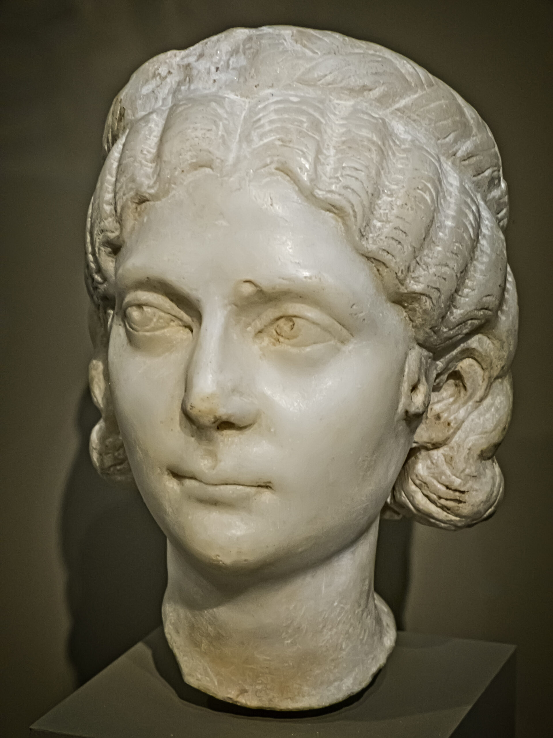 Marble bust of a woman with center-parted wavy hair in soft curls, calm expression, and detailed features against a neutral background.