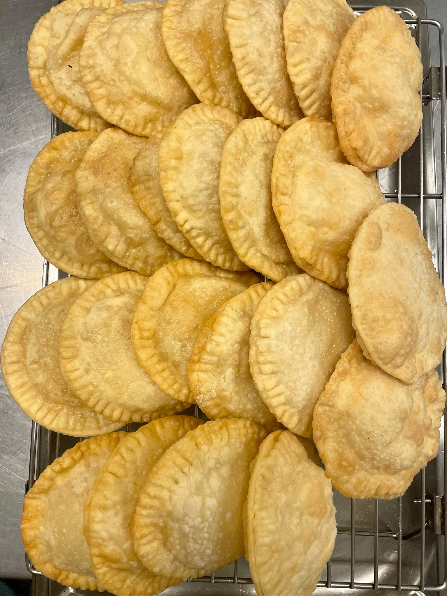 A tray of golden-brown, half-moon fried pastries arranged in neat, overlapping rows atop a wire cooling rack.