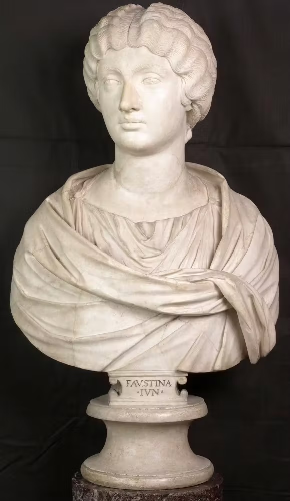 Marble bust of a woman with braided wavy hair in a robe. “FAUSTINA IVN.” inscribed on the pedestal, black background enhances detail.