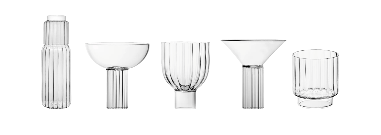 Five clear glassware pieces with vertical ribbing—a carafe, coupe, goblet, martini glass, and tumbler—lined up on white.