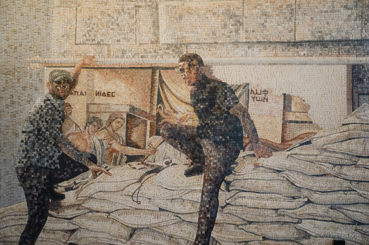 Un mosaico mostra due uomini su pile di sacchi, uno che fa un passo avanti, l'altro che tende la mano; un terzo lavora accanto a una parete con manifesti e scritte.