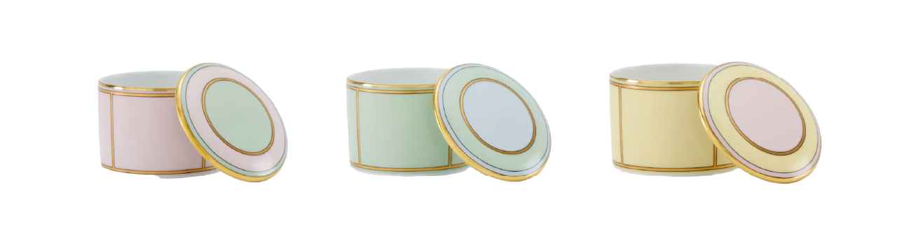 Three round pastel porcelain boxes—pink, green, yellow—with gold accents. Lids rest by each box on a white background.